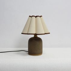 a lamp that is sitting on top of a white surface with a brown base and beige lampshade