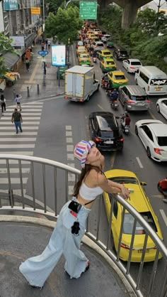 a woman standing on the side of a metal railing next to a street filled with traffic