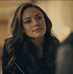 a woman with long dark hair is looking at something in the distance while sitting down