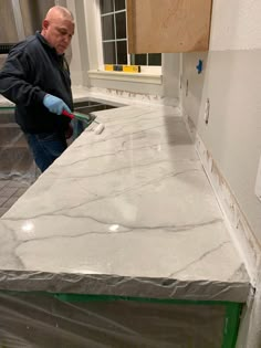 a man standing next to a counter in a kitchen with white marble on the counter