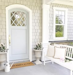 two white benches sitting in front of a door with flowers on the bench next to it