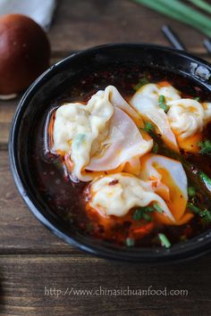 some dumplings are in a black bowl on a wooden table