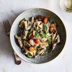 a bowl filled with pasta and vegetables on top of a white table next to a fork