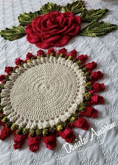 crocheted doily with red flowers and green leaves on a white tablecloth