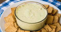 a white plate topped with crackers next to a glass filled with dip and cheese