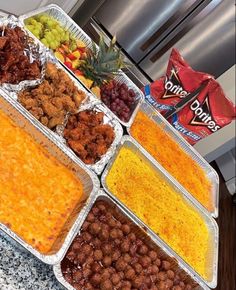 several trays of food sitting on top of a counter next to a bag of chips