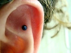 a close up view of a person's ear with a tiny blue dot on it