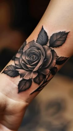 a black and white rose tattoo on the left arm, with leaves around it's edges