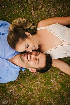 a man and woman laying on the grass together smiling at each other's eyes