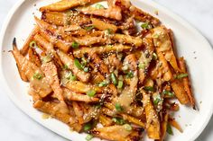 a white plate topped with french fries covered in sauce and green onion sprinkles