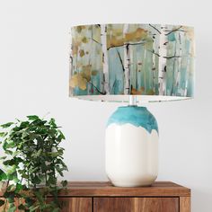 a table lamp sitting on top of a wooden cabinet next to a potted plant