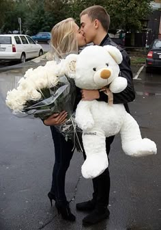 a man kissing a woman while holding a teddy bear in front of her on the street