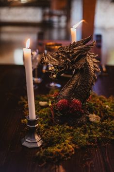 a dragon figurine sitting on top of a moss covered table next to a candle