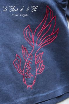 a blue shirt with a red fish embroidered on it