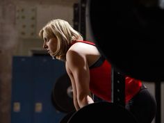 a woman squatting down in front of a barbell with one hand on her hip