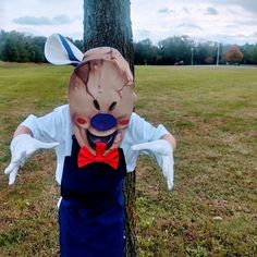 a person wearing a creepy mask and bow tie standing next to a tree in a field