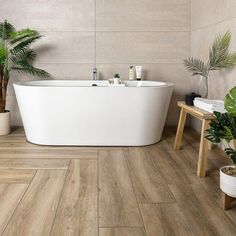 a white bath tub sitting on top of a wooden floor next to potted plants