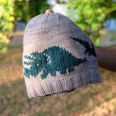 a hand holding a knitted hat with green trees on the front and back of it