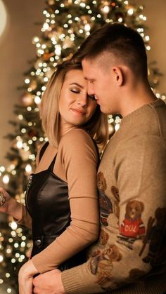 a man and woman standing next to each other in front of a christmas tree with lights