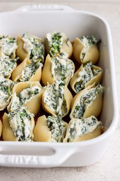 a white casserole dish filled with spinach and pasta shells covered in sauce