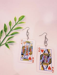 two playing cards are hanging from earrings next to a green plant on a white surface