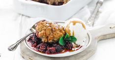 a white plate topped with fruit cobbler next to a serving dish filled with ice cream