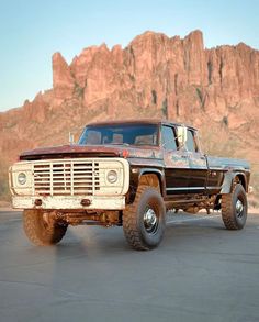 an old pick up truck parked in front of a large rock formation with mountains in the background