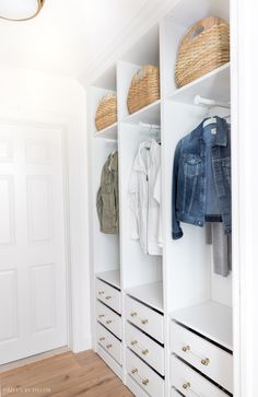 a white closet with clothes and baskets on top of the shelves, next to a door