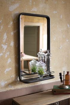 a mirror is hanging on the wall above a shelf filled with jars and glassware