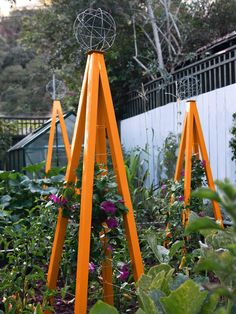 an orange metal sculpture stands in the middle of a garden with purple flowers and greenery