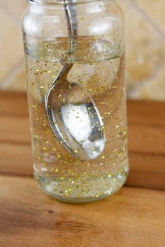 a jar filled with liquid sitting on top of a wooden table next to a spoon