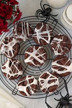 chocolate cookies with white icing are on a cooling rack next to a red flower