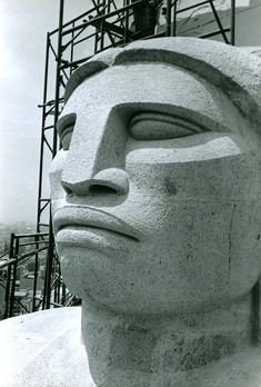 a large statue with a man on top of it's head and scaffolding in the background