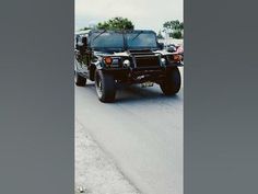 a large black truck driving down a street next to another vehicle on the side of the road