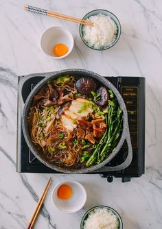 a pan filled with meat and vegetables on top of a table next to bowls of rice