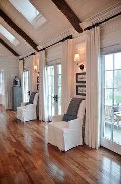 a living room filled with white furniture and wooden flooring next to two large windows