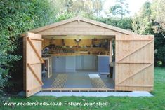 a wooden shed with the doors open and shelves on it's side, in front of some trees