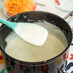 a wooden spoon in a pot filled with liquid and cheese gravy on a colorful tablecloth