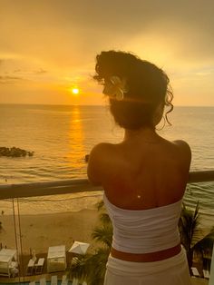 the back of a woman in a white dress looking out over the ocean at sunset