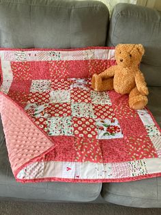 a teddy bear sitting on top of a pink quilted blanket next to a couch