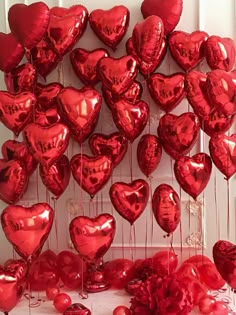 a bunch of red heart shaped balloons hanging from the side of a wall with strings