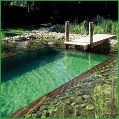 a wooden dock sitting on top of a river next to a lush green field with rocks and grass