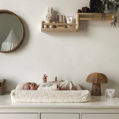 a baby laying on top of a white bed next to a wall mounted clock and shelf