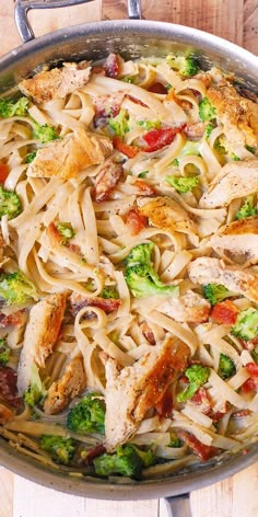 a skillet filled with chicken, pasta and broccoli on top of a wooden table