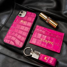 a pink leather case and keychain on top of a black bag next to a cell phone