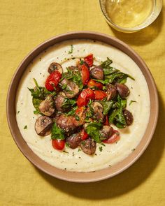 a bowl of soup with mushrooms, tomatoes and spinach on it next to a glass of beer