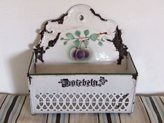 a white and green box with an ornate design on the lid sitting on a striped tablecloth