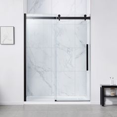 a white bathroom with a glass shower door and marble tile flooring on the walls