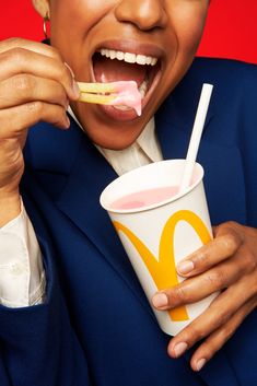 a woman in a blue jacket is brushing her teeth and holding a drink with a toothbrush