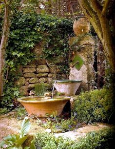 an outdoor fountain in the middle of a garden with plants growing around it and stone walls